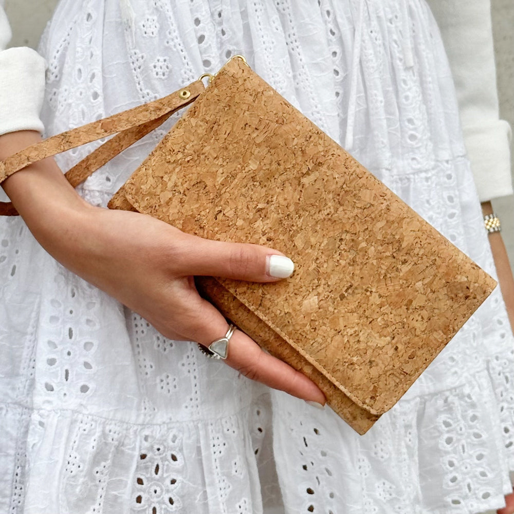 Model in white dress holding wrist strap of By The Sea Collection, Lyla, classic vegan cork leather clutch