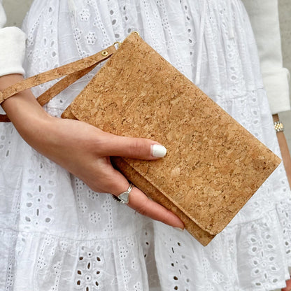 Model in white dress holding wrist strap of By The Sea Collection, Lyla, classic vegan cork leather clutch